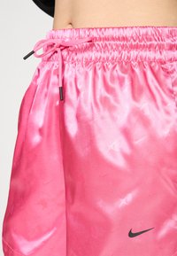 Rosa, sateng sportshorts med drawstring midje, med et subtilt Nike-logo og mønster. Glatt tekstur; lett design.