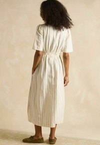 Balti svītrota midi kleita ar īsām piedurknēm un savilkta jostas vieta, ar sānu kabatām un brīvu piegriezumu, kopā ar olīvu zaļām kurpēm.