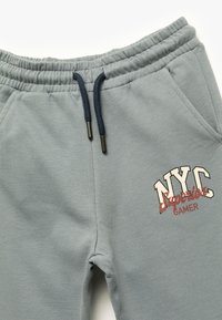 Graue Jogginghosen mit einem elastischen Bund und dunkelblauen Kordeln, vorderen Taschen und einem bedruckten Design mit der Aufschrift "NYC Superior Gamer."