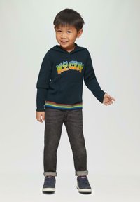 Navy gebreide hoodie met "NY CITY" graphic in gradient kleuren, kangoeroezak, gestreepte ribs aan de onderkant. Gecombineerd met donkere jeans en sneakers.