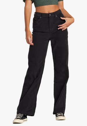 Pantalones de pana negra con cintura alta, piernas anchas, cierre de botón y bolsillos laterales; tejido texturizado con costillas verticales.