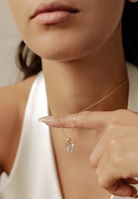 Collana con pendente a forma di farfalla in oro con accenti di pietre preziose trasparenti, appesa a una delicata catena attorcigliata, presentata su uno sfondo chiaro.