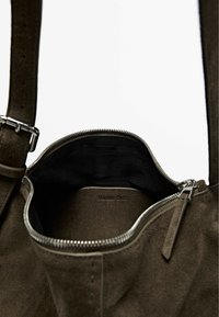 Brown suede handbag interior with a black lining and zipper closure. Features a logo embossed on the inner wall and a textured strap.