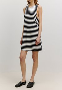 Pasiasta, bezrękawnikowa sukienka w granatowo-białym kolorze, charakteryzująca się luźnym krojem i okrągłym dekoltem, uzupełniona prostymi czarnymi butami.