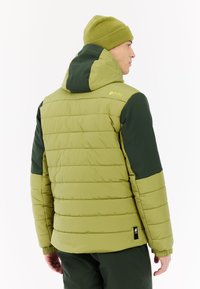 Zelena podstavljena jakna s kapuljačom, koja ima teksturiranu površinu i ušivenu konstrukciju. Akcenti uključuju tamnozelene dijelove na ramenima i logo.