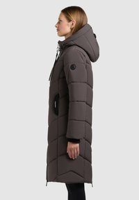 Grau gepuffte Jacke mit Kapuze, ausgestattet mit einem gesteppten Design, schwarzen Akzenten, seitlichen Taschen und einer langen Silhouette.
