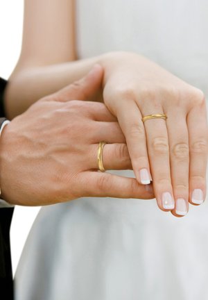 Two hands are shown, one wearing a smooth gold band and the other with a twisted gold ring. Nails are painted with a French manicure.