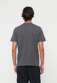 Czarnoszary t-shirt z okrągłym dekoltem i krótkimi rękawami. Gładka bawełniana tkanina, dopasowany krój, bez widocznych logo ani wzorów na plecach.