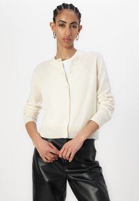Cardigan couleur crème en tricot doux, avec un col rond et une fermeture par boutons, doté de poignets et d'un ourlet côtelés.