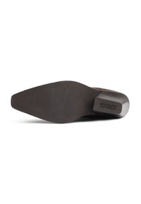 Zapato de cuero marrón de punta afilada visto desde la suela, con un tacón cuadrado y el nombre de la marca "BRONX" estampado.
