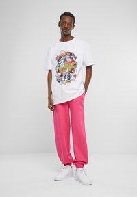 Hvid t-shirt med et farverigt tegneserieprint på forsiden, parret med løstsiddende lyserøde sweatpants og hvide sneakers.