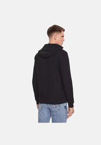 Sudadera negra con un corte relajado, con capucha ajustable, mangas largas y tela suave. Combinada con jeans de color azul claro.