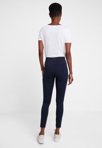Leggings navy en tissu extensible, conçus avec une taille haute, associés à un haut blanc à manches courtes. Texture lisse, coupe ajustée.