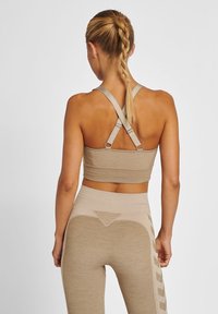 Beige sportbehå med korskrafter och texturerad linning, som är kombinerad med högmidjade tights med geometriska detaljer och en slät yta.