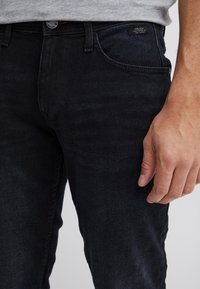 Fekete egyenes szabású farmernadrág finom textúrával, öt zsebbel és a derékrészen jól látható márkajelzéssel.