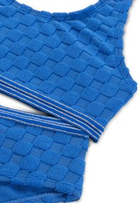 Kék textúrájú crop top, amely kockás mintázattal rendelkezik, sima szalaggal, amelyet két ezüst csík díszít az alján.