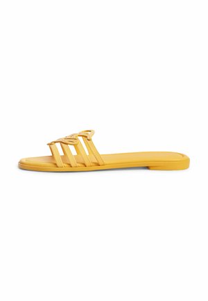 Gelbe flache Sandale mit drei dünnen Riemen und dekorativem ausgeschnittenem Schmetterlingsdetail auf weißem Hintergrund.