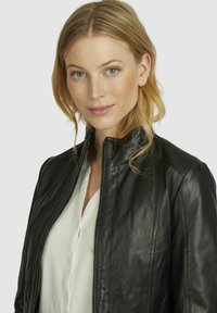 Black leather jacket with a high collar, zip front, and soft texture; worn over a white button-up shirt.