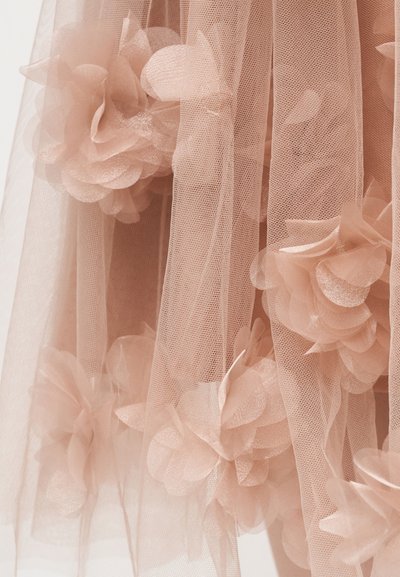 Λεπτό τούλι σε ροδακινί απόχρωση με στρωματοποιημένες εφαρμογές λουλουδιών, δημιουργώντας ένα απαλό, υφασμένο και ρέον διακοσμητικό μοτίβο.