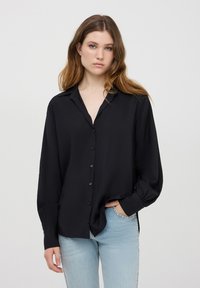 Camicetta nera con bottoni realizzata in tessuto liscio, dal taglio morbido, maniche lunghe e colletto, abbinata a jeans azzurri chiari.