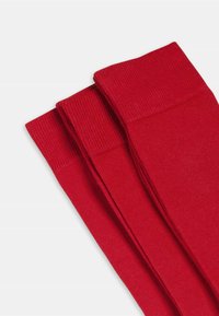 Calze rosse a coste alte fino al ginocchio con una texture liscia, caratterizzate da un ampio risvolto a coste e tre paia impilati insieme.