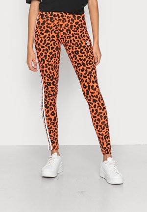 Oranje legging met een zwart luipaardpatroon, witte zijstrepen en een hoge tailleband. Geschikt met witte sneakers.