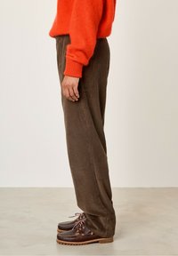 Brahno kordurojske hlače s ravnim nogavicami, ki imajo teksturirane brazde in sproščen kroj, v kombinaciji s temno rjavimi čevlji.