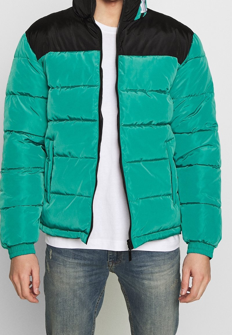 Tealfärgad puffjacka med svart övre panel, blixtlåsstängning och ribbade mudd. Slät textur med horisontell quiltning och fickor.