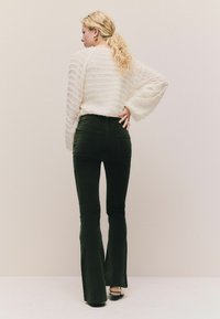 Hvid, struktureret striktrøje med horisontale striber; parret med sorte flagrende jeans; model vender væk, poserer mod en neutral baggrund.