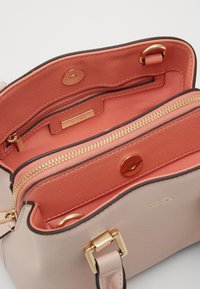 Jasnoróżowa torebka o gładkiej powierzchni z kontrastową koralową podszewką, złotymi okuciami i zamykanymi na zamek przedziałami. Posiada magnetyczne zapięcie.