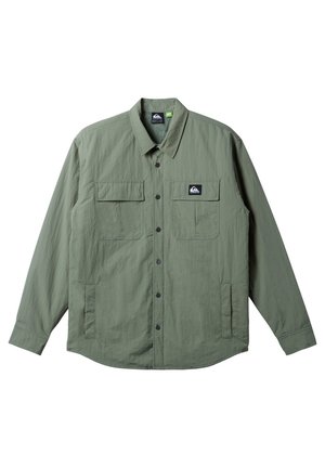 Light green long-sleeve shirt made from a textured fabric, featuring two chest pockets, a button placket, and a branded logo patch.
