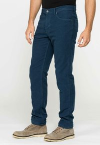 Chinos blu navy realizzati in tessuto misto cotone; design slim fit con tasche anteriori e chiusura a bottone. Indossati con stivali alla caviglia beige.