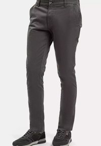 Szare spodnie o prostym kroju, wykonane z gładkiego materiału. Zawierają przednie kieszenie i zapięcie na guzik, zestawione z czarnymi trampkami.