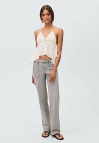 Bijela halter top majica s čvorom sprijeda, uparen s svijetlosivim trapericama sa širokim nogavicama i crnim japankama.