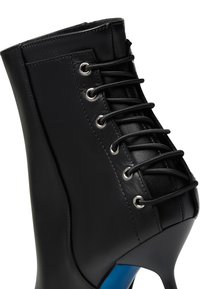 Stivale ankle in pelle nera con tacco alto, caratterizzato da una parte anteriore con lacci, occhielli metallici e un design a pannelli testurizzati.