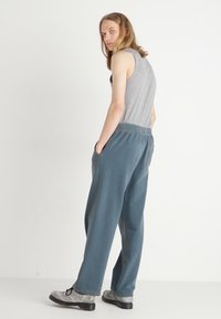 Luftige blaue Hosen mit strukturierter Oberfläche, ausgestattet mit Seitentaschen und einem elastischen Bund, kombiniert mit einem grauen Tanktop.