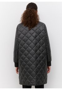 Sort quiltet overtøj med en lang silhuet, der har diamantmønstre, ribstrikkede manchetter og en glat, skinnende tekstur.