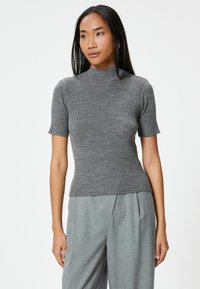 Kurzärmliges, geripptes graues Oberteil mit hohem Kragen und figurbetontem Schnitt, aus weichem Strickmaterial gefertigt, kombiniert mit grauen maßgeschneiderten Hosen.