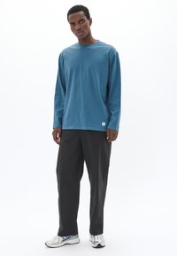 Blaues Langarmhemd aus weichem Stoff, kombiniert mit lockeren schwarzen Hosen und silbernen Sportschuhen, mit einem minimalistischen Design.