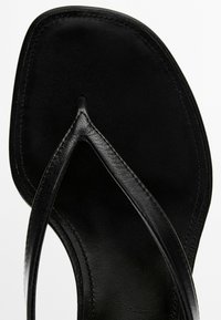 Sort læderflip-flop sandal med firkantet tå og synlige syninger rundt om kanterne mod en hvid baggrund.