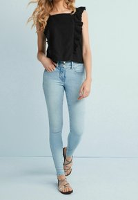 Sort ærmeløs top med flæsedetaljer, parret med lyseblå skinny jeans og snørebåndsandaler med en fletdesign.