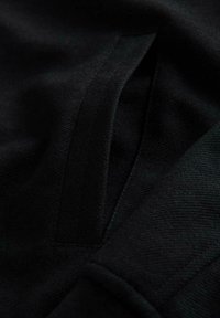 Czarna tkanina o gładkiej, lekko teksturowanej powierzchni. Posiada ukrytą kieszeń ze starannie stworzonym szwem. Brak wzorów ani akcesoriów.