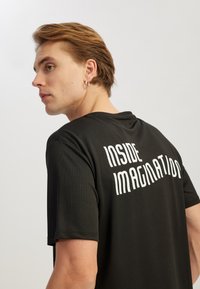 Sort kortærmet T-shirt lavet af tekstureret stof med et iøjnefaldende hvidt print på ryggen, der står "INSIDE IMAGINATION."