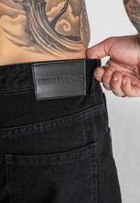 Zwarte denim jeans met een leren taillepatch met de tekst "GIANNI KAVANAGH." Kenmerken zijn onder andere gestikte zakken en een nauwsluitend ontwerp.