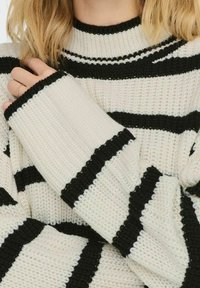 Schwarz-weißer gestreifter Strickpullover mit hohem Kragen und weiten Ärmeln mit gerippten Bündchen, der ein strukturiertes Stoffmuster zeigt.