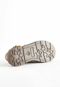Semelle de chaussure avec une surface en caoutchouc beige texturé. Motif d'étoiles remarquable et rainures pour l'adhérence. Contient une zone de flex rectangulaire.