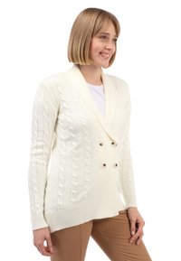 Crème kleur kabelgebreide cardigan met een dubbelzijdig ontwerp, voorzien van grote bruine knopen en ribbels aan de manchetten. Gladde textuur, lange mouwen.