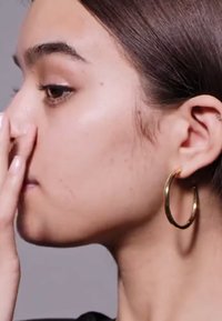 Gullørering, stor sirkulær design. Glatt tekstur, skinnende overflate. Nærbilde av sideprofil med hånden berørende kinnet.