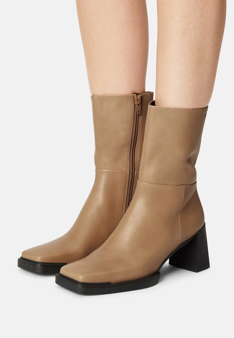 Skórzane, beżowe botki za kostkę z kwadratowym noskiem i szerokim obcasem. Posiadają boczny zamek błyskawiczny i gładką fakturę.