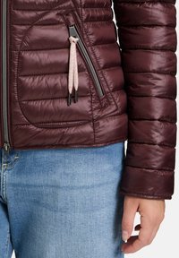 Bordeaux pufferjakke med quiltet tekstur, sidelomme med lynlås og snoredetaljer. Sammen med lyseblå denimjeans.